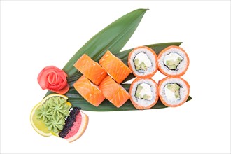 Overhead view of sushi roll with raw salmon fillet on top with avocado served on bamboo leaves