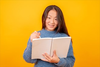 Studio photo with yellow background of a chinese woman holding a notebook while studying