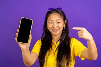 Studio photo with purple background of a chinese woman pointing to the screen of a mobile phone