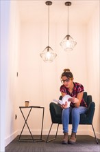 Vertical portrait of a young woman reading a book at home in a cozy corner of a room