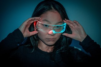 Studio photo with blue background with neon lights of a chinese woman with cybernetic glasses looking at camera