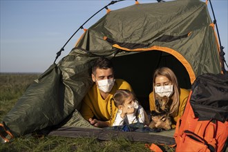 Family wearing masks sitting tent with their dog front view