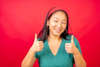 Studio photo with red background of a smiling chinese woman gesturing agreement with thumbs up