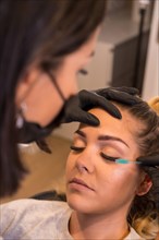 Vertical photo of a professional applying mascara to the eyelashes of the beautiful woman in the beauty salon