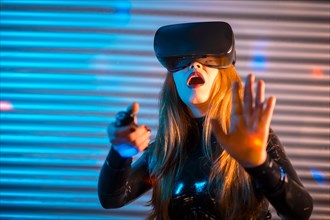 Surprised woman wearing virtual reality goggles and gesturing in an urban night space with neon lights