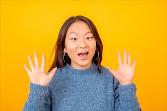 Studio photo with yellow background of a surprised chinese young woman looking at camera