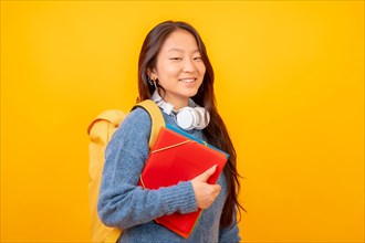 Studio photo with yellow background of a chinese student with headphones