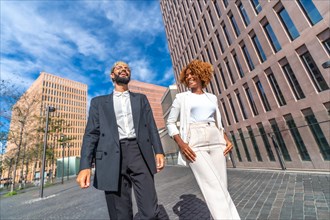 Dynamic and low angle view photo of two multi-ethnic young business people walking distracted along a financial neighborhood