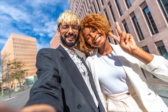 Low angle view and frontal view photo of a businessman and businesswoman talking a selfie smiling and gesturing success outdoors