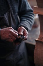 Senior violinmaker wrinkled old hands holding a tool chisel in workshop in Cremona