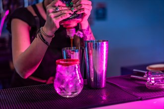 Bartender mixing ingredients in a cocktail mixer in the counter of a bar with neon lights