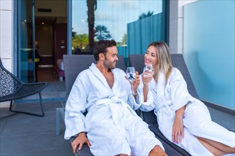 Happy couple toasting with wine sitting on a lounge outdoors in a luxury spa