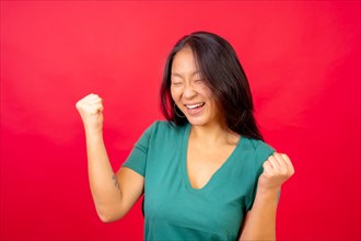 Studio photo with red background of a chinese woman celebrating raising fist with eyes closed