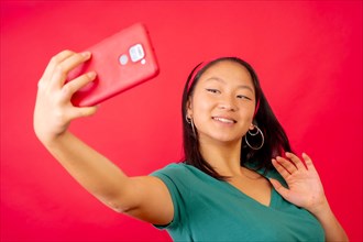 Studio photo with red background of a happy chinese woman waving during a video call