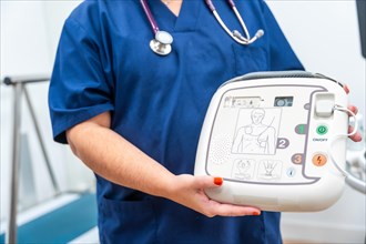 Close-up photo of a cardiologist holding a defibrillator and explain how to use it
