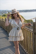 Vertical portrait of a woman wearing summer dress and hat posing next to the sea