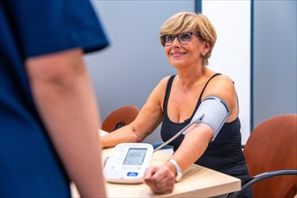 Smiling mature woman sitting during a blood pressure exam in a cardiology clinic