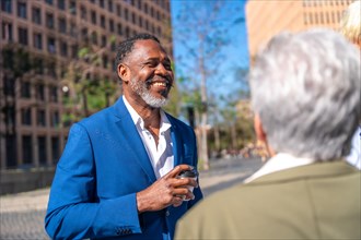 African mature businessman talking with colleagues drinking take away coffee relaxed and smiling outdoors