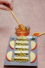 Woman sprinkles a wooden spoon with honey on a tray with cheese