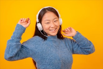 Asian woman dancing with white headphones looking at camera on a yellow background