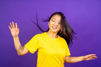 Studio photo with purple background of a young casual chinese woman dancing happily