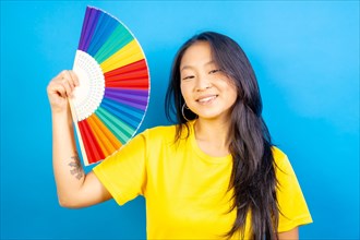 Studio photo with blue background of a chinese woman using a rainbow colored folding fan