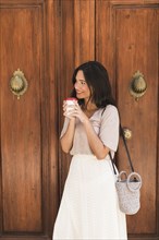 Side view girl standing front door holding disposable coffee cup