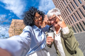 Happy multi-ethnic businesswomen taking a funny selfie gesturing with hands standing on the street
