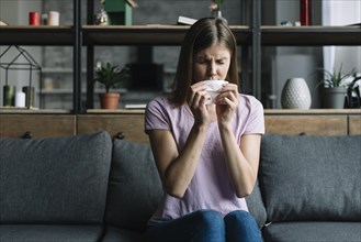 Woman sitting sofa blowing nose with tissue paper