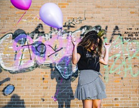Girl holding balloons front graffiti wall