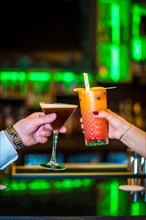 Vertical close-up of two people toasting with luxury cocktails in a bar