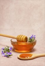 Honey in a glass bowl with a wooden spoon and fresh rosemary sprigs in bloom