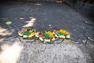 Three beautiful colourful opera bowls on the roadside. Flowers as an offering in Ubud
