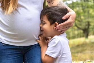 Tender image of a kid embracing the belly of his pregnant mother outdoors