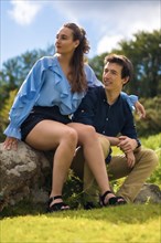 Vertical photo of a stylish young couple looking aside sitting on the mountain