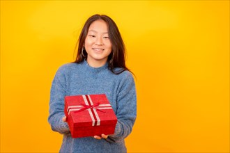 Studio photo with yellow background of a chinese woman giving a present smiling at camera