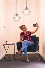 Smart girl taking a selfie with mobile sitting in a cozy room at home