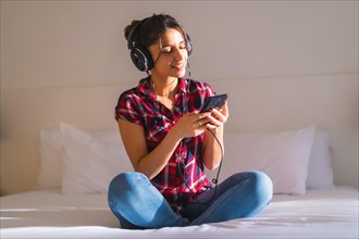 Frontal portrait of a young woman listening to music sitting on a bed