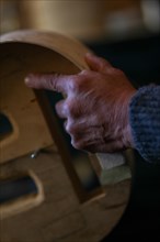 Luthier artisan violin maker wrinkled hand hold carve sculpt chisel ribs of a new classical model cello in workshop Cremona Italy