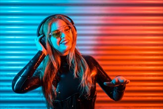 Blonde disc jockey using headphones in an urban space with colorful neon lights