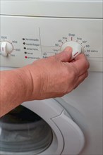 Woman hand choosing program on automatic washing machine for laundry at home. Turning knob on control panel