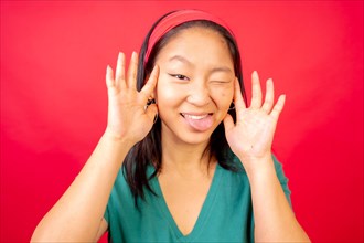 Studio photo with red background of a funny chinese young woman pulling faces and gesturing