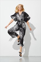 Fashion model in patterned overall jumping in bright studio