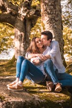 Vertical photo of a young man embracing and kissing his girlfriend sitting on the forest