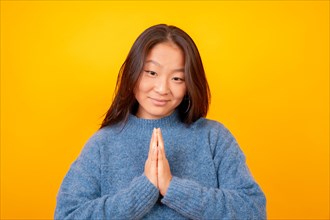 Asian woman making the please gesture looking at camera on a yellow background