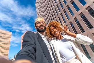 Low angle view portrait of two successful business colleagues smiling and taking a selfie outdoors in a sunny day in the city