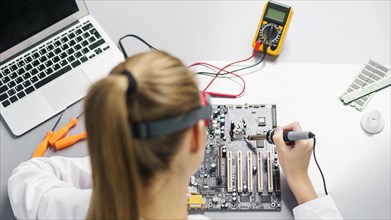 High angle female technician with soldering iron electronics motherboard