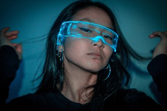Studio photo with blue background with neon lights of a cool chinese woman using futuristic smart goggles