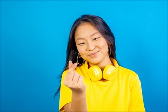 Studio photo with blue background of a chinses woman symbolizing heart with an asian traditional gesture