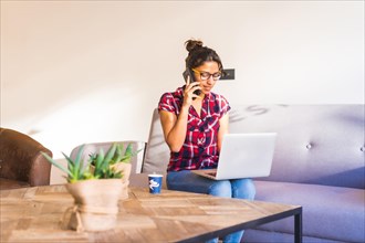Woman using phone while working on remote using laptop sitting on a sofa